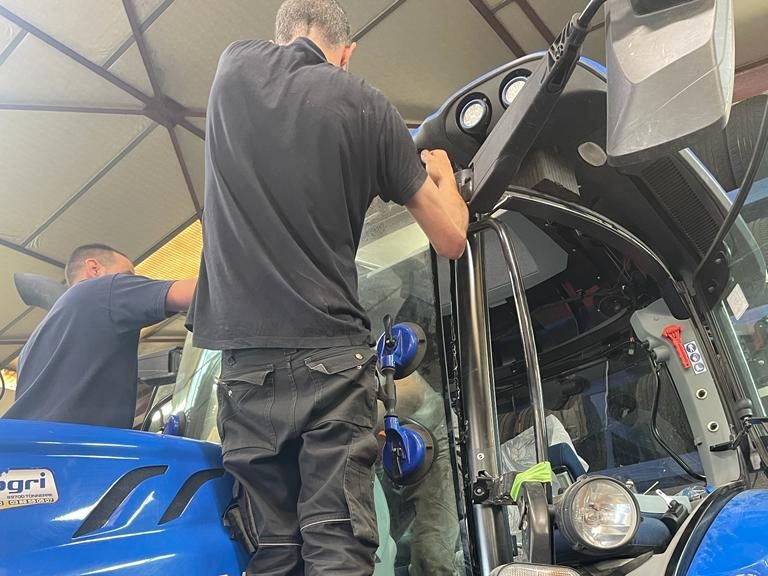 Remplacement du pare-brise d'un tracteur New Holland T6.125S à deux techniciens dans l'atelier Formula Pneus Point S à Sens