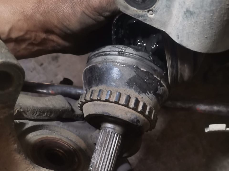 Cardan désaccouplé du moyeu à l'atelier : joint homocinétique et couronne ABS couverts de graisse noire échappée du soufflet déchiré — Formula Pneus à Sens